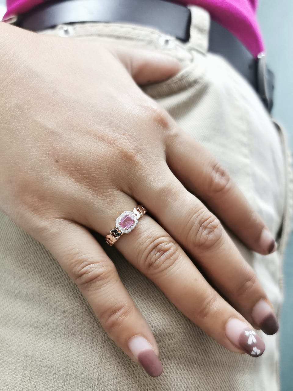 Elegant 18K gold pink sapphire and diamond halo ring with a 0.50-carat emerald-cut pink sapphire, surrounded by 0.14-carat round diamonds and a chain-link band design.