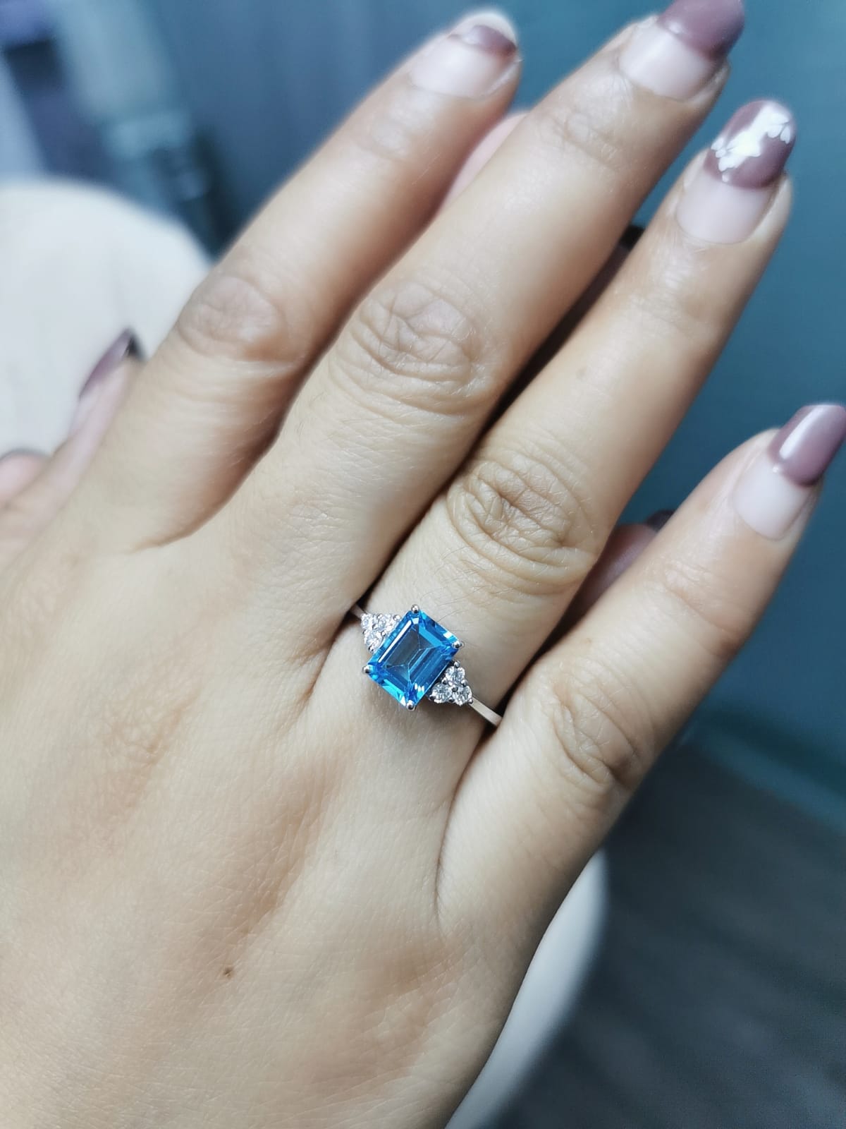 Elegant Swiss Blue Topaz and diamond ring in 18K gold, featuring a 1.66-carat emerald-cut Swiss Blue Topaz flanked by 0.17-carat diamonds in a classic three-stone design.