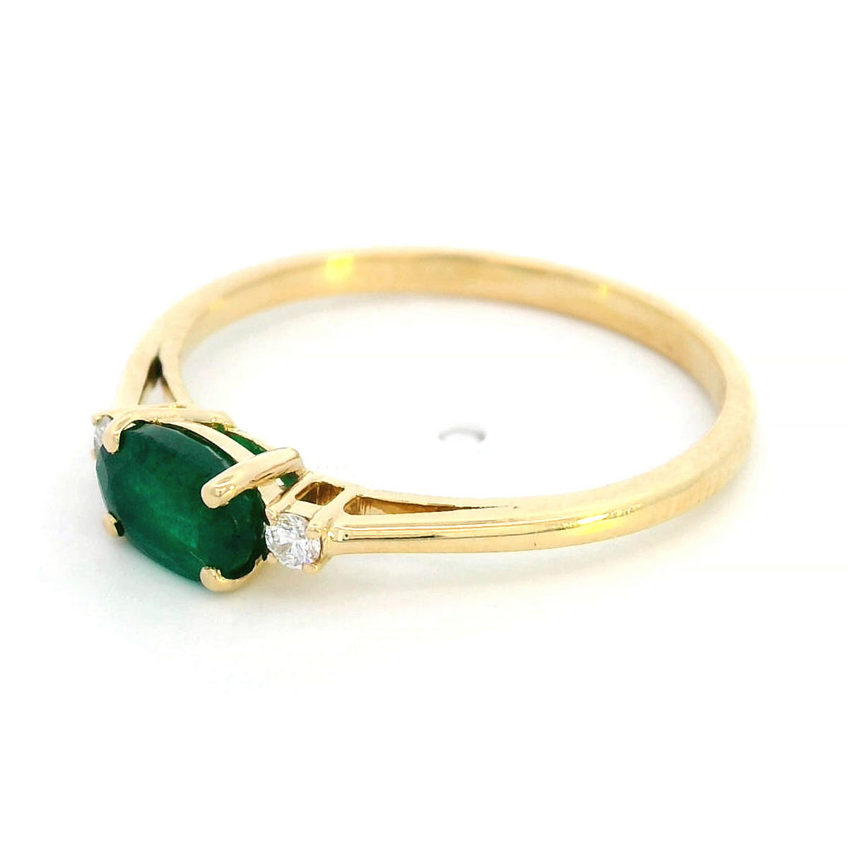 18K yellow gold oval emerald and diamond ring featuring a 0.59-carat emerald with 0.05-carat round diamonds on each side in a classic four-prong setting.