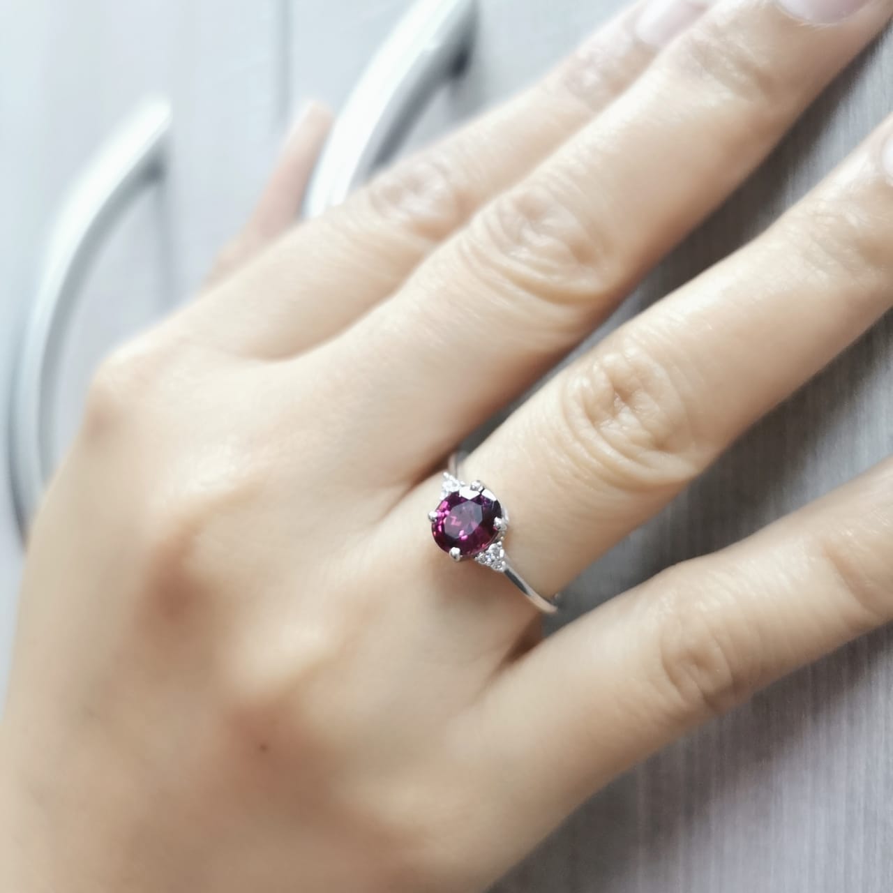 18K white gold ring featuring a 1.71-carat oval rhodolite garnet with three round-cut diamond accents (0.06 CT total) on a polished band.