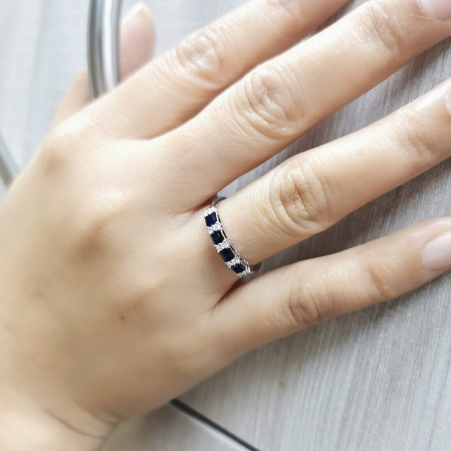 18K white gold sapphire and diamond eternity ring featuring princess-cut blue sapphires and round white diamonds in a half-eternity design.