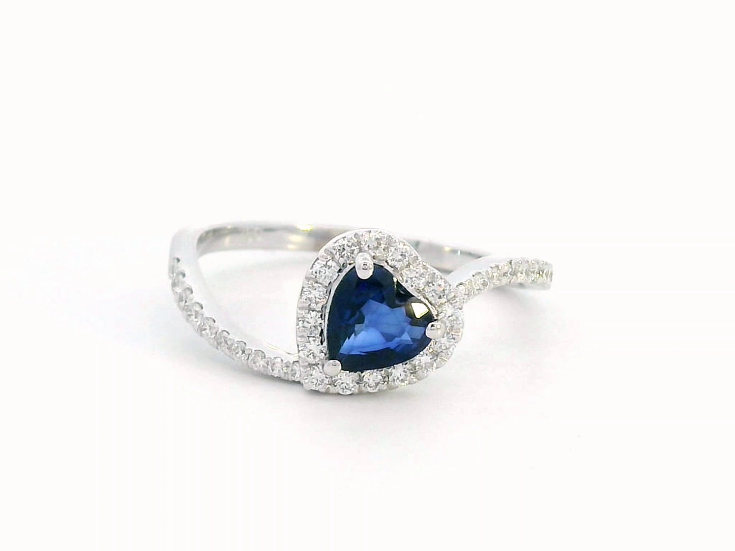 Heart-cut blue sapphire ring with diamond halo set in 18K gold, featuring a bypass design for a romantic touch.