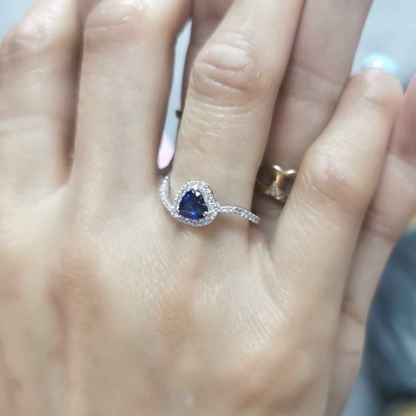 Heart-cut blue sapphire ring with diamond halo set in 18K gold, featuring a bypass design for a romantic touch.