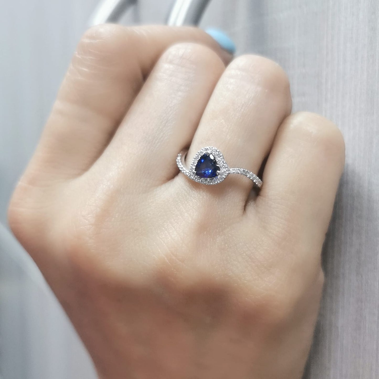 Heart-cut blue sapphire ring with diamond halo set in 18K gold, featuring a bypass design for a romantic touch.