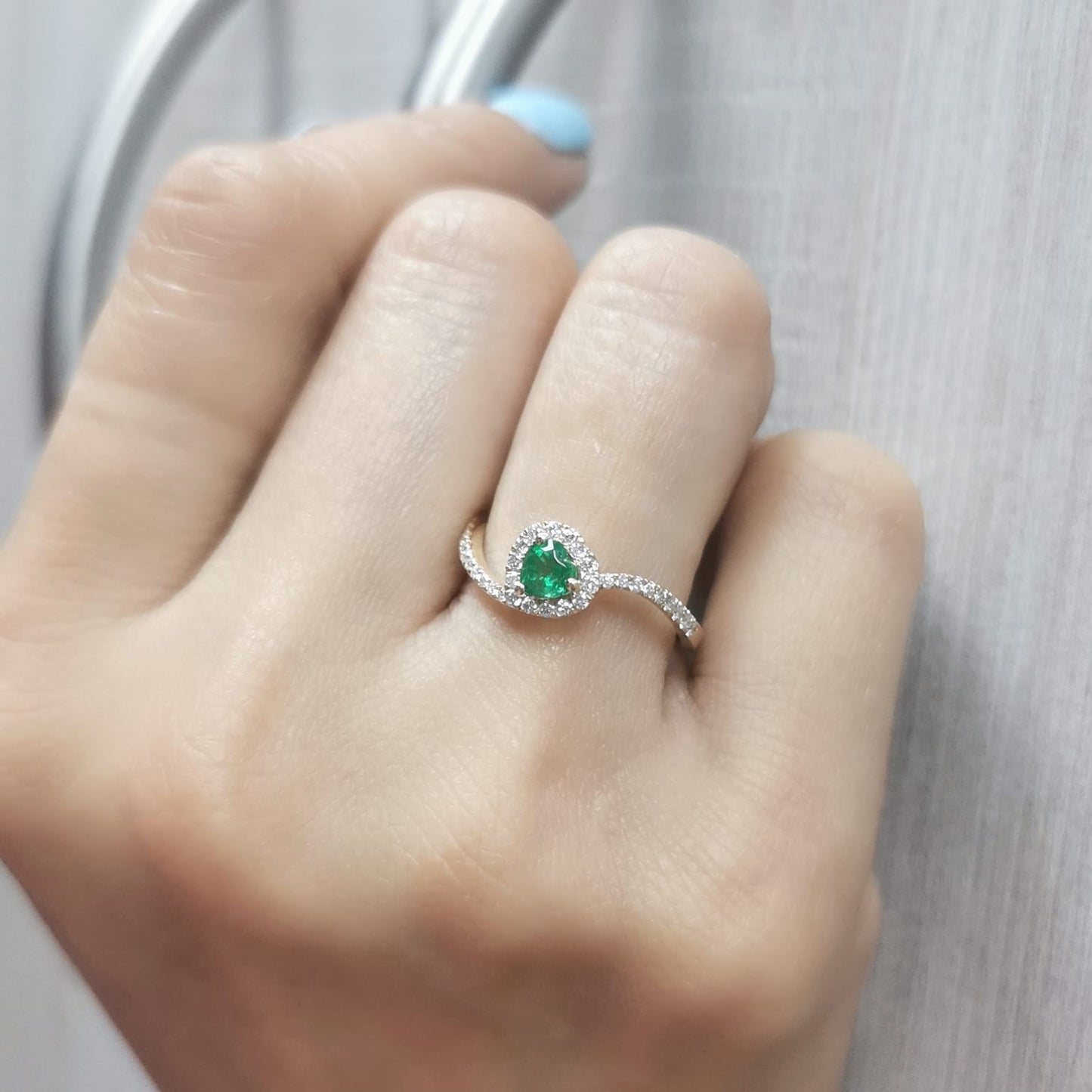 Heart-cut emerald ring with a diamond halo in 18K gold, featuring a bypass design for a timeless and elegant look.