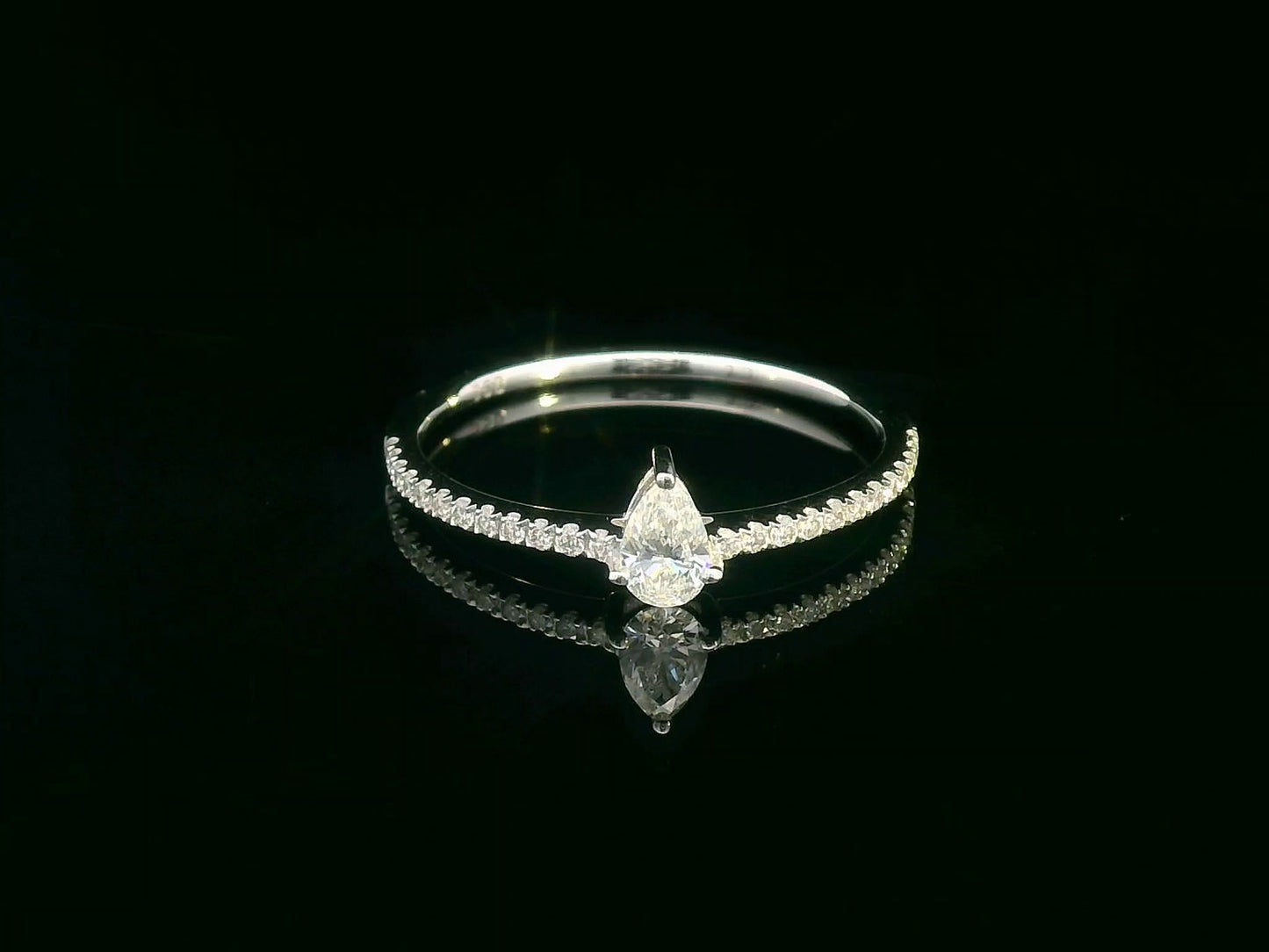 Slim 18K gold ring with pear-shaped diamond and pavé band, minimalist fine jewelry.