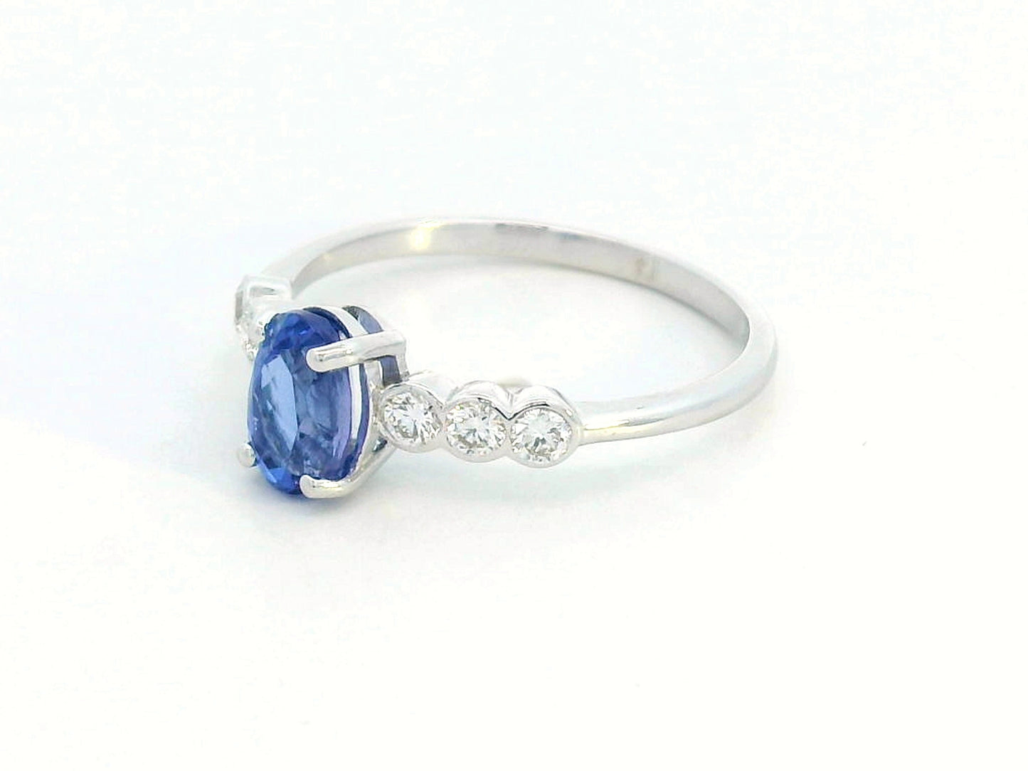 Oval tanzanite and diamond ring in 18K white gold with bezel-set side stones