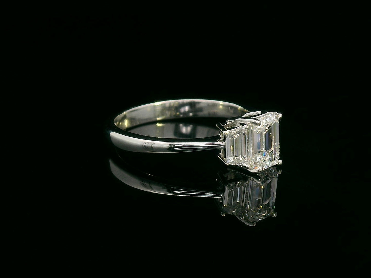 Three-stone engagement ring with emerald-cut center diamond and trapezoid side diamonds in 18K gold