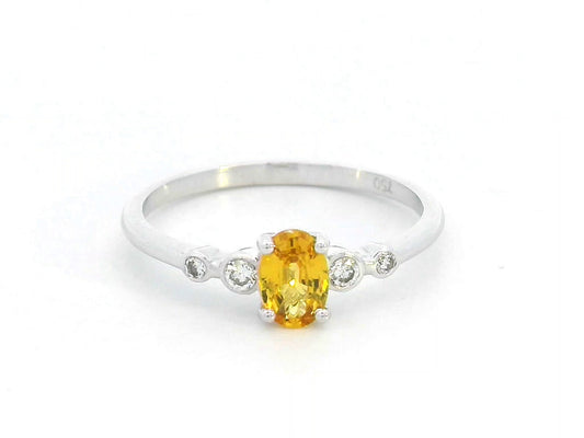 18K gold ring with 0.48ct oval yellow sapphire and two bezel-set round diamonds on a polished band.