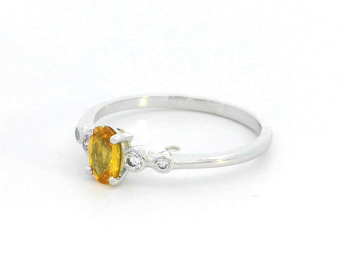 18K gold ring with 0.48ct oval yellow sapphire and two bezel-set round diamonds on a polished band.