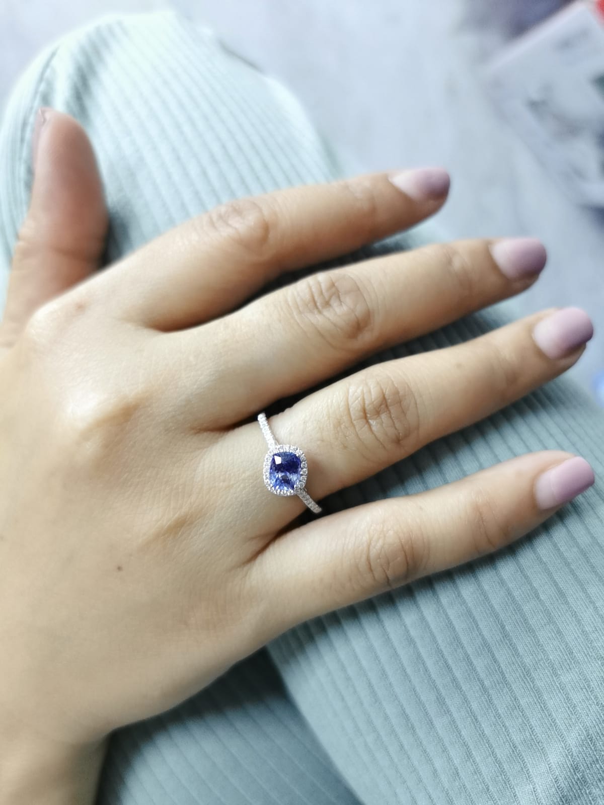 Hand wearing a ring with a blue gemstone on a light gray fabric background
