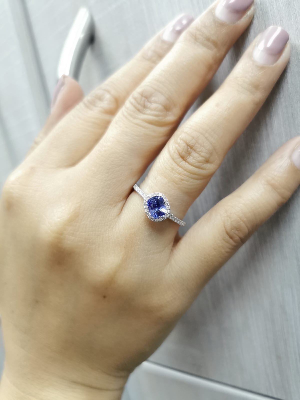 Hand wearing a ring with a blue gemstone on a neutral background