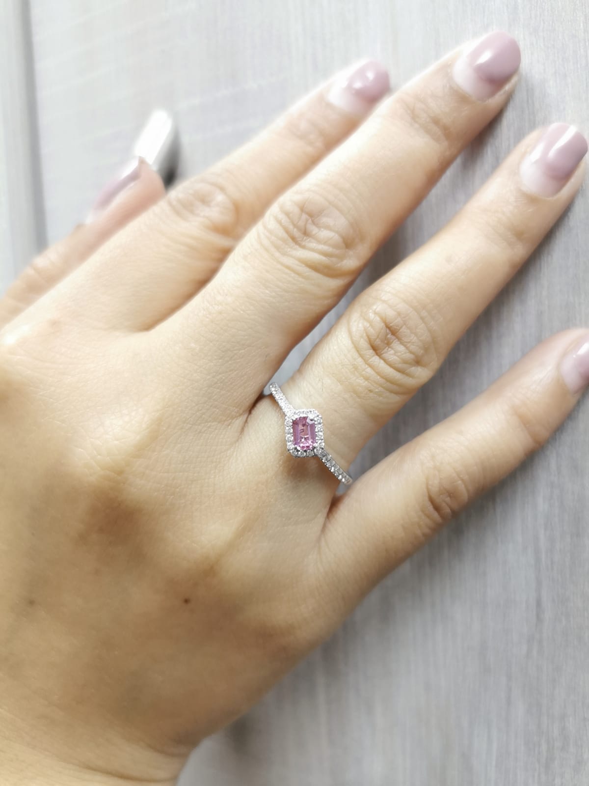 Hand wearing a ring with a pink gemstone on a light wooden surface