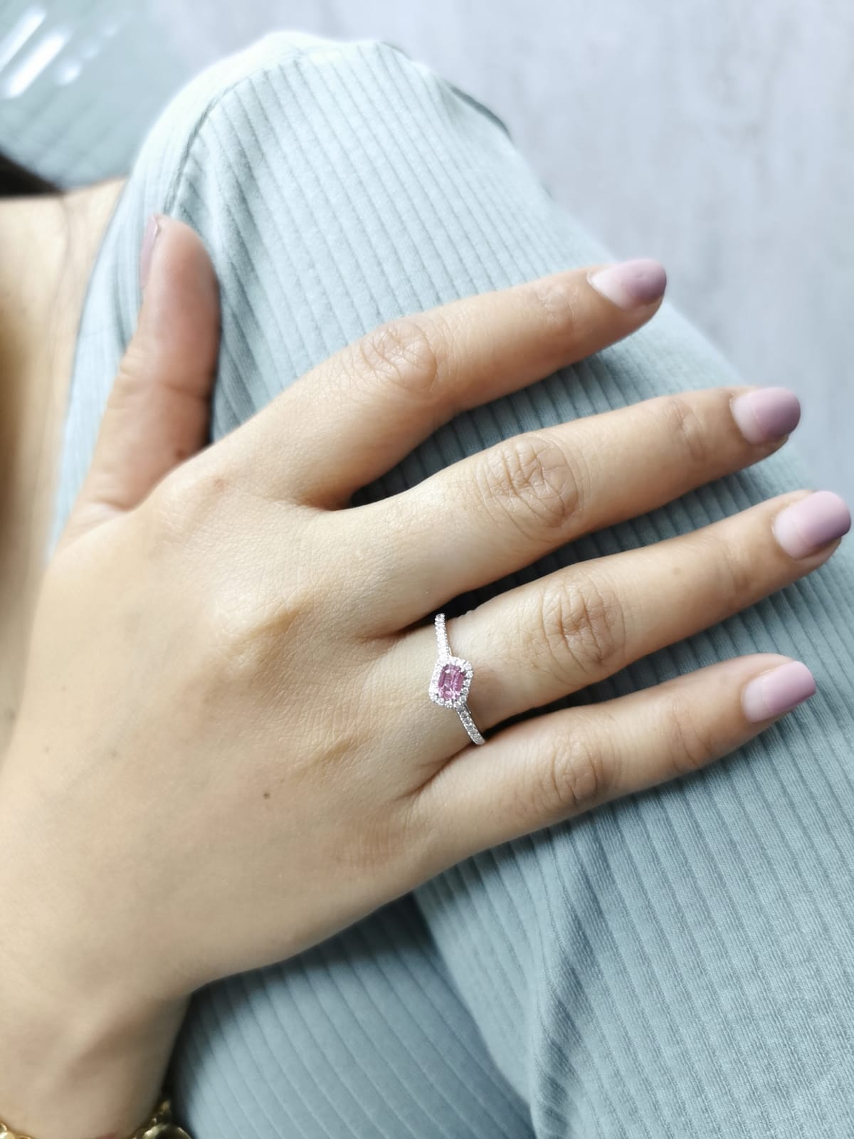 Hand wearing a ring with a pink gemstone on a light gray background