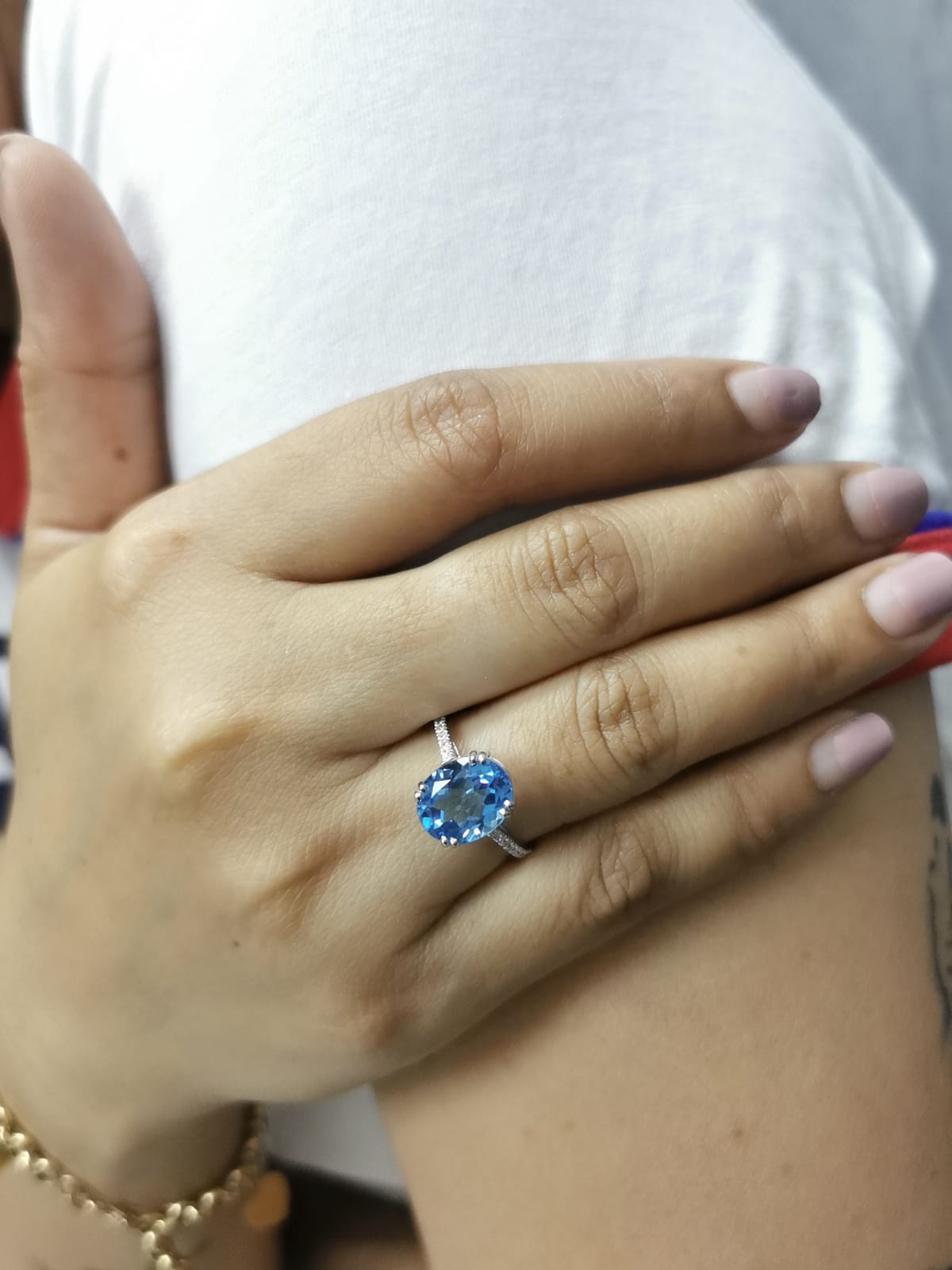 Hand wearing a ring with a blue gemstone against a white background