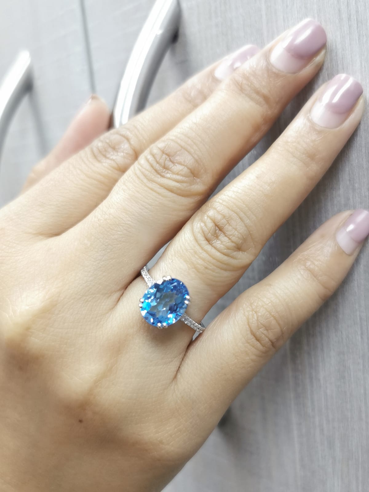 Hand wearing a ring with a blue gemstone on a neutral background