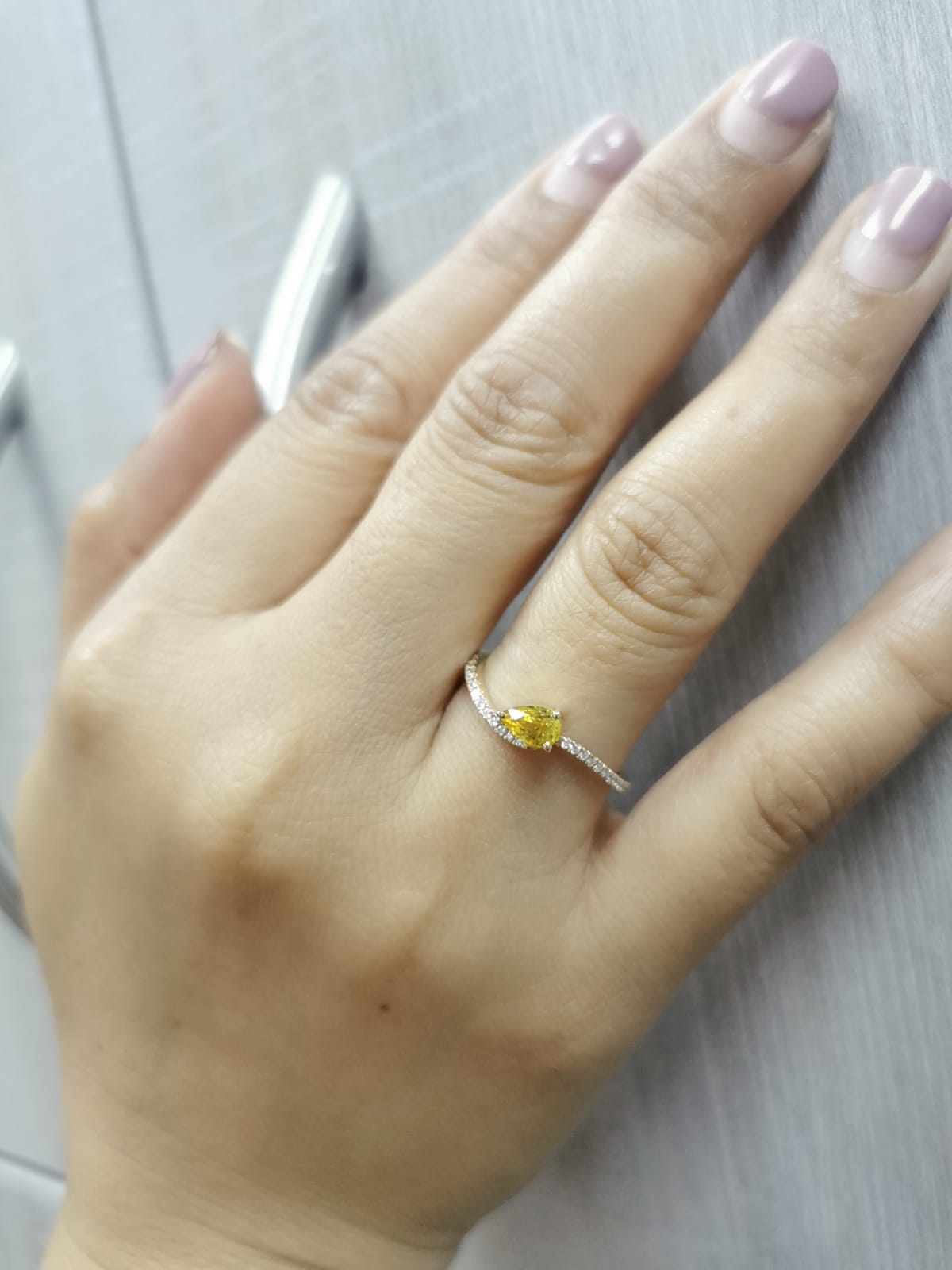 Hand wearing a ring with a yellow gemstone on a light gray background