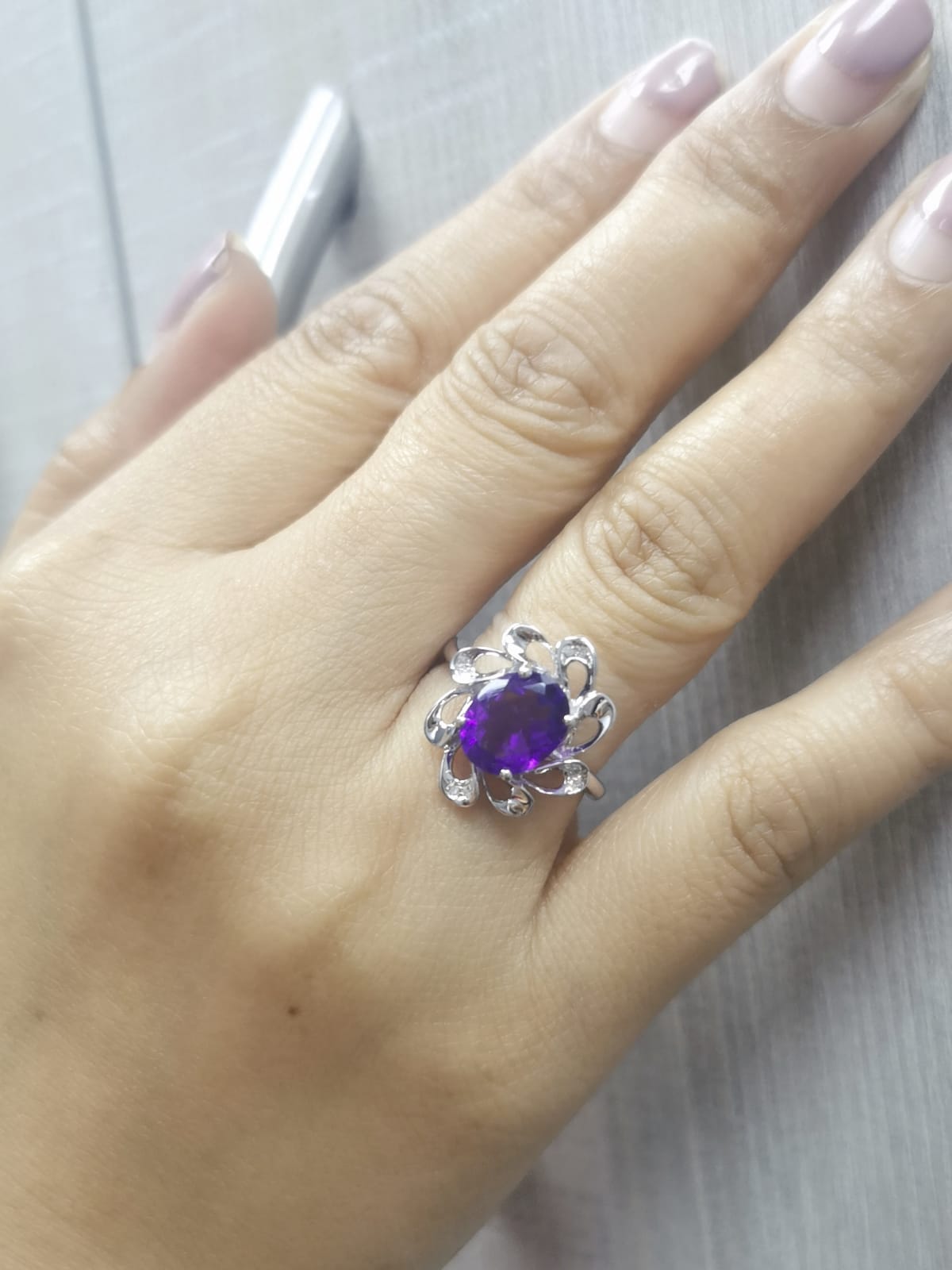 Hand wearing a white gold ring with a purple gemstone on a light gray background