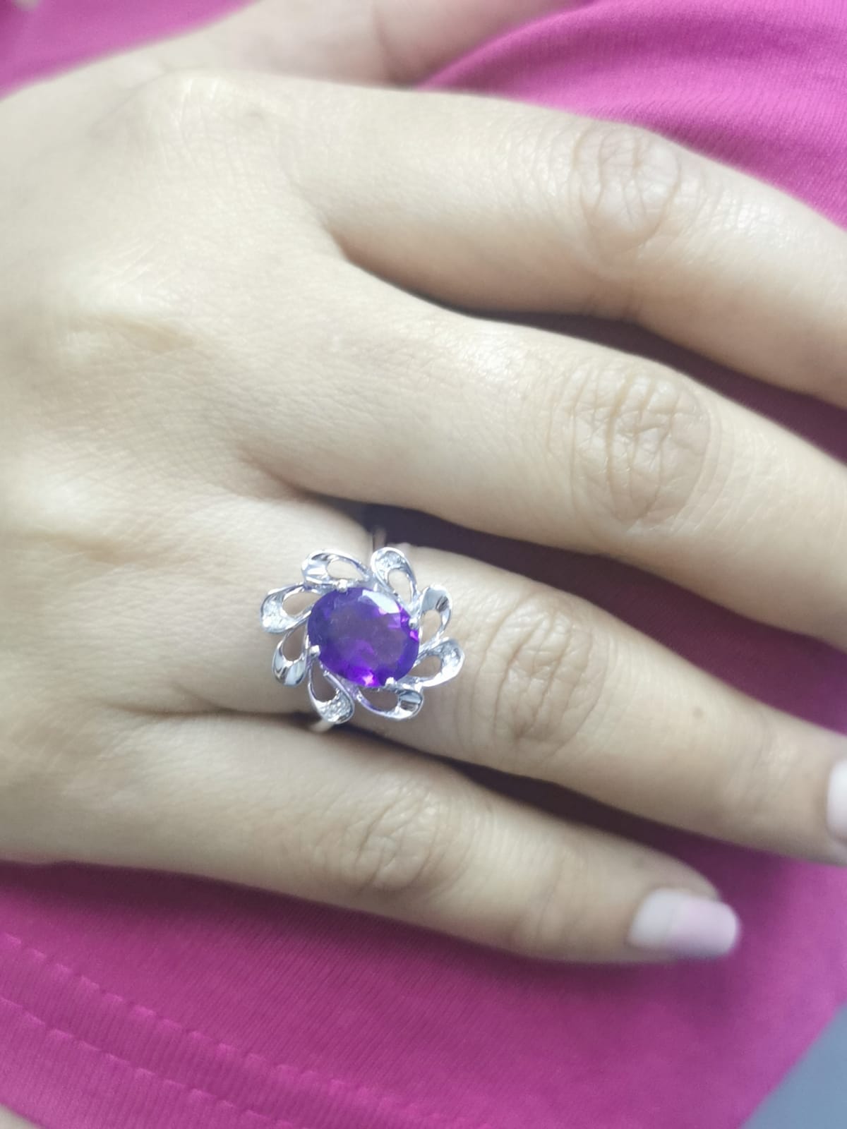 white gold ring with a purple gemstone on a hand against a pink background