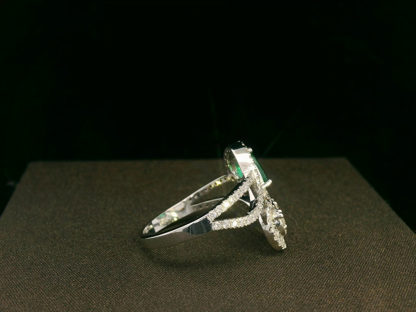 18k gold bypass ring with 0.59 ct pear-cut emerald, pear-shaped diamond cluster, and pavé diamonds, modern asymmetrical design.