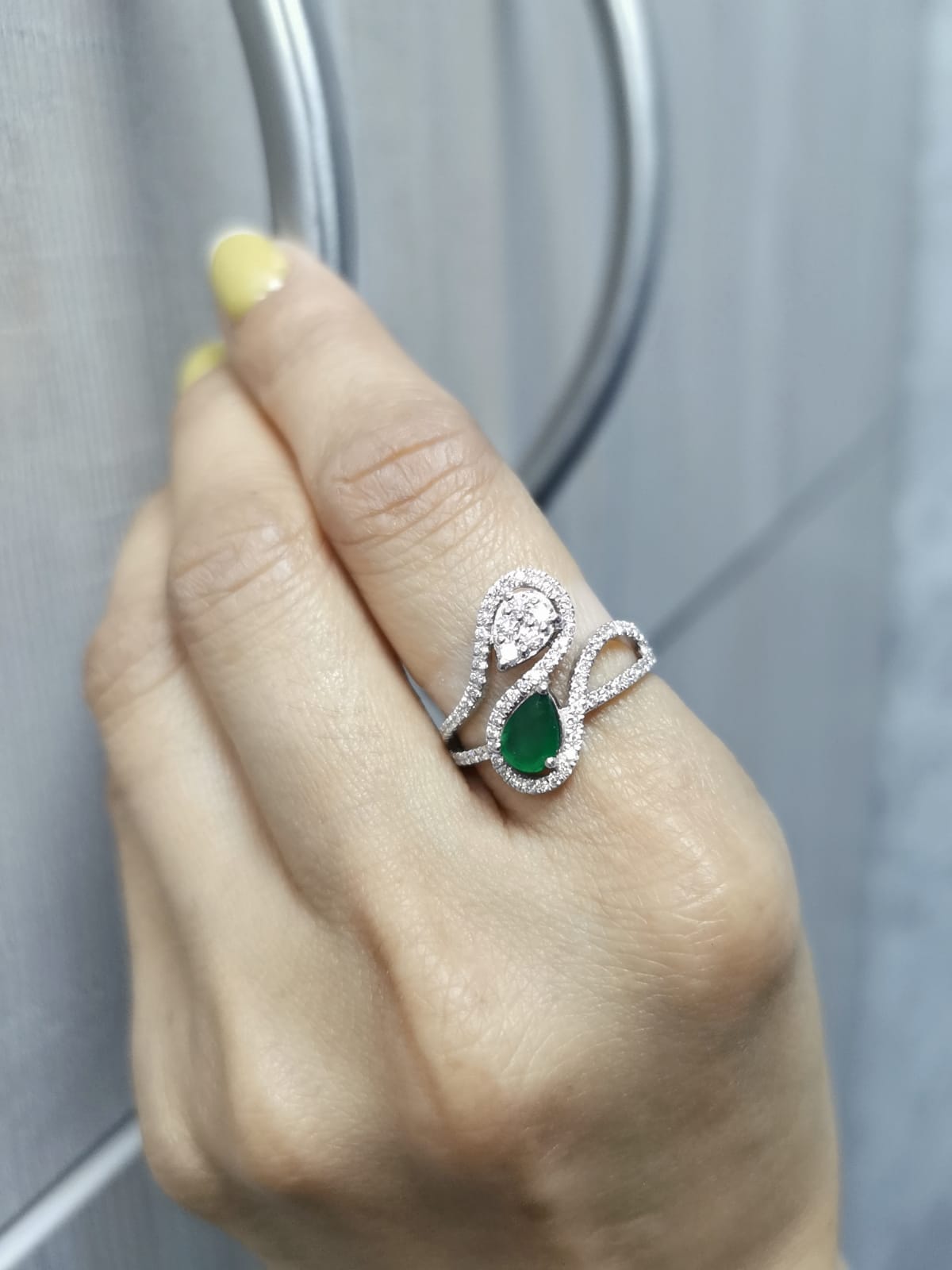 18k gold bypass ring with 0.59 ct pear-cut emerald, pear-shaped diamond cluster, and pavé diamonds, modern asymmetrical design.