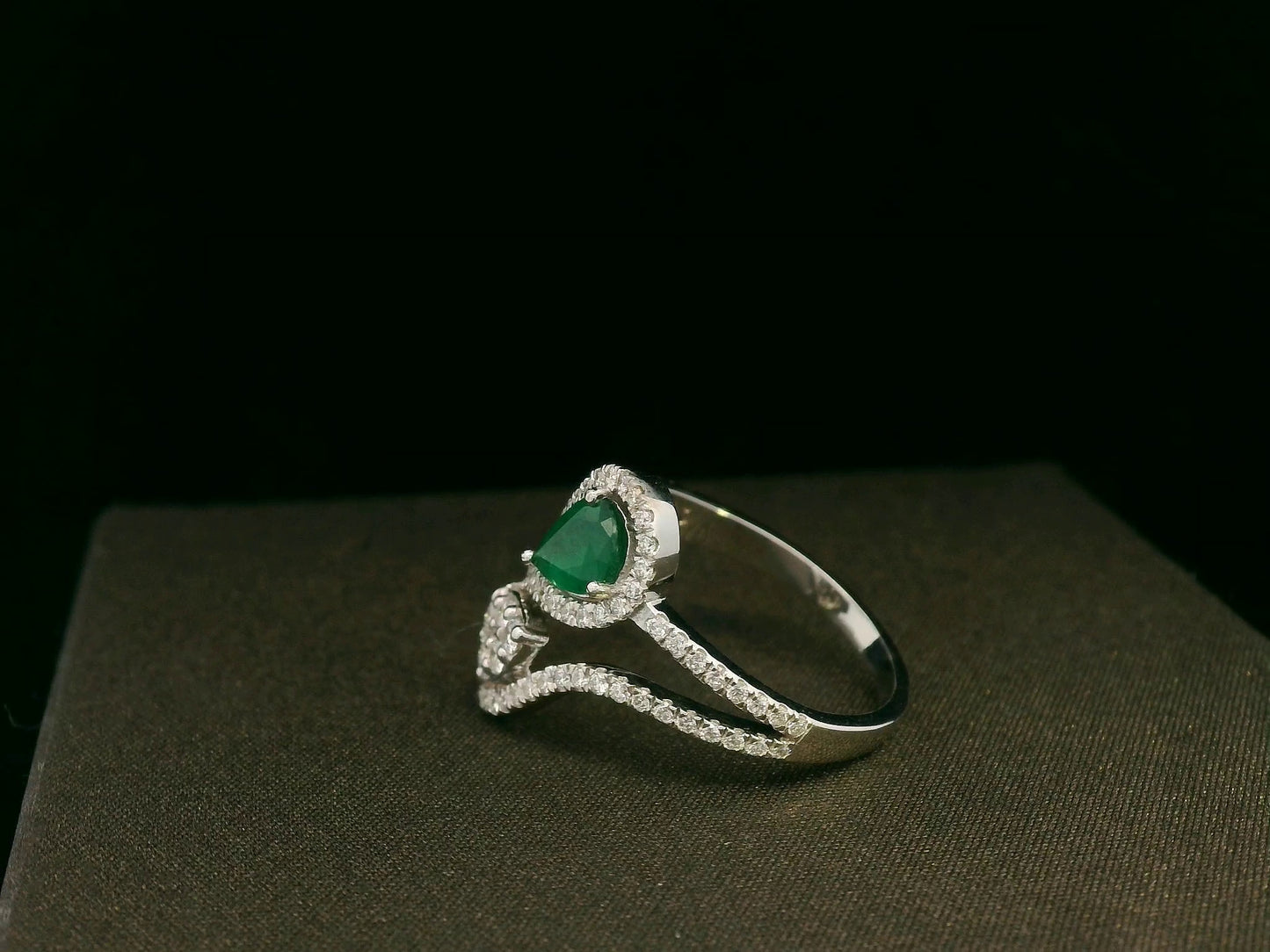 18k gold bypass ring with 0.59 ct pear-cut emerald, pear-shaped diamond cluster, and pavé diamonds, modern asymmetrical design.