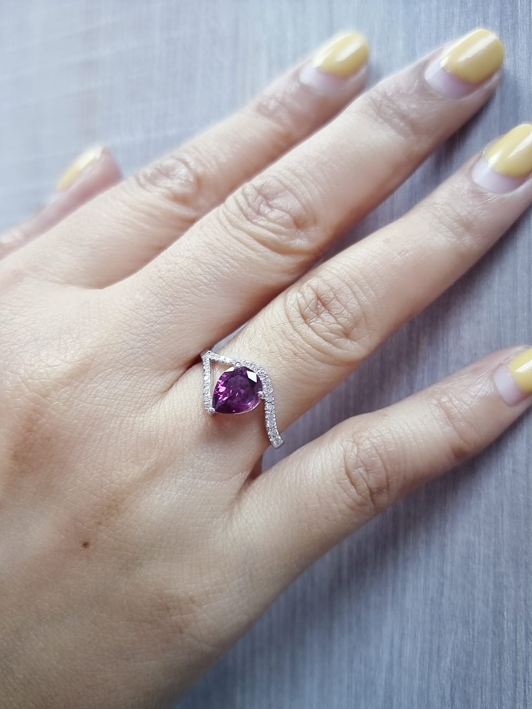18K white gold rhodolite garnet and diamond wave ring featuring a 1.97ct pear-cut garnet framed by 0.23ct pavé diamonds in an elegant wave design.
