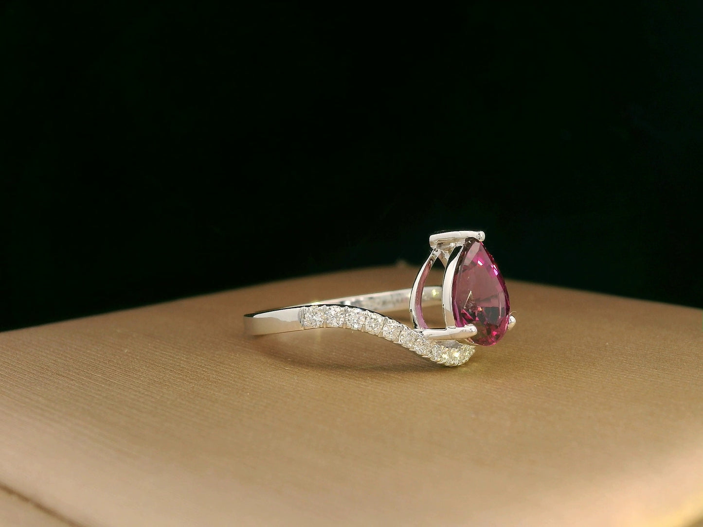 18K white gold rhodolite garnet and diamond wave ring featuring a 1.97ct pear-cut garnet framed by 0.23ct pavé diamonds in an elegant wave design.