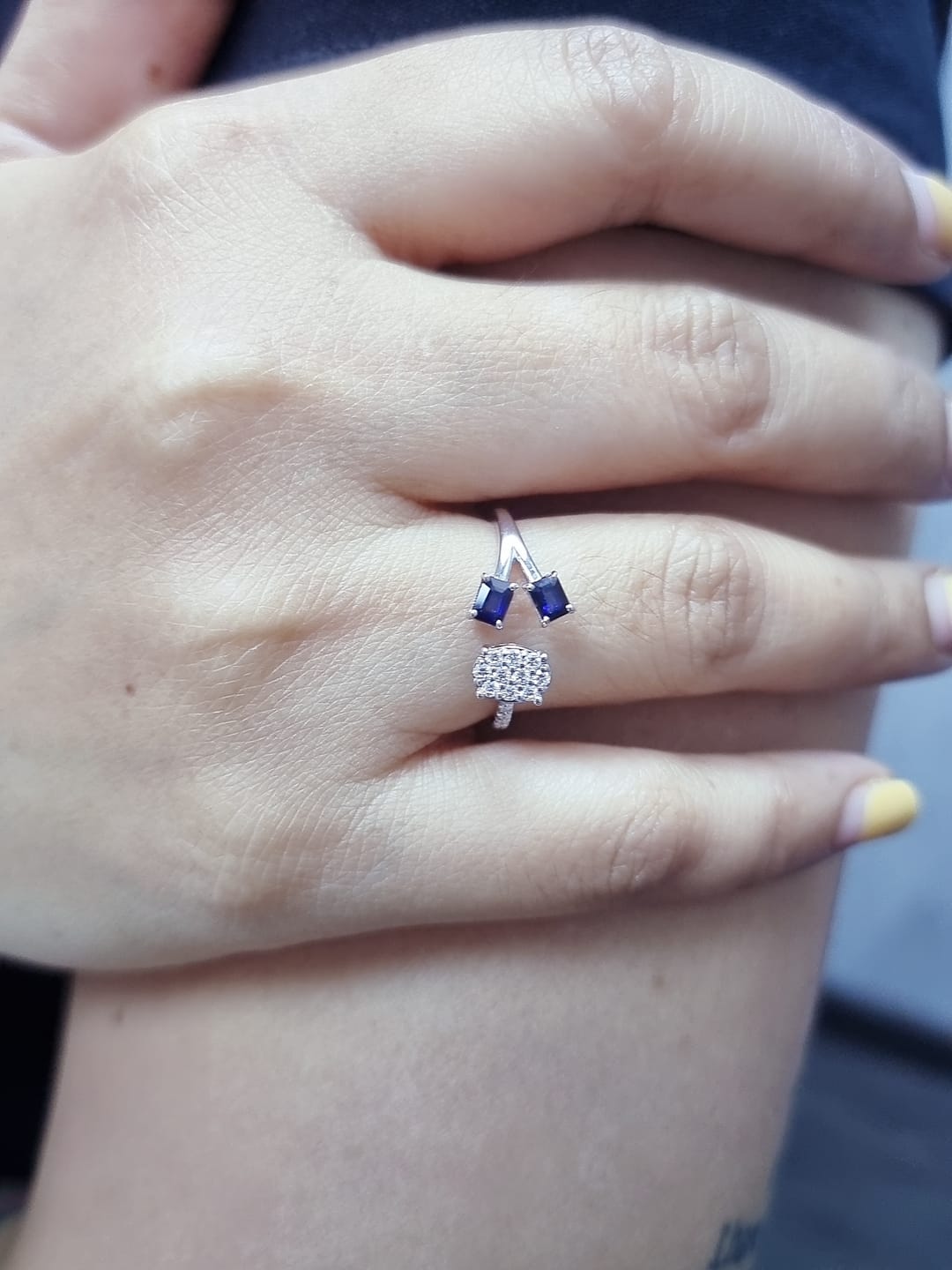 18K white gold open-shank ring featuring an oval diamond cluster on one side and two emerald-cut blue sapphires on the other, accented with pavé diamonds along the band.
