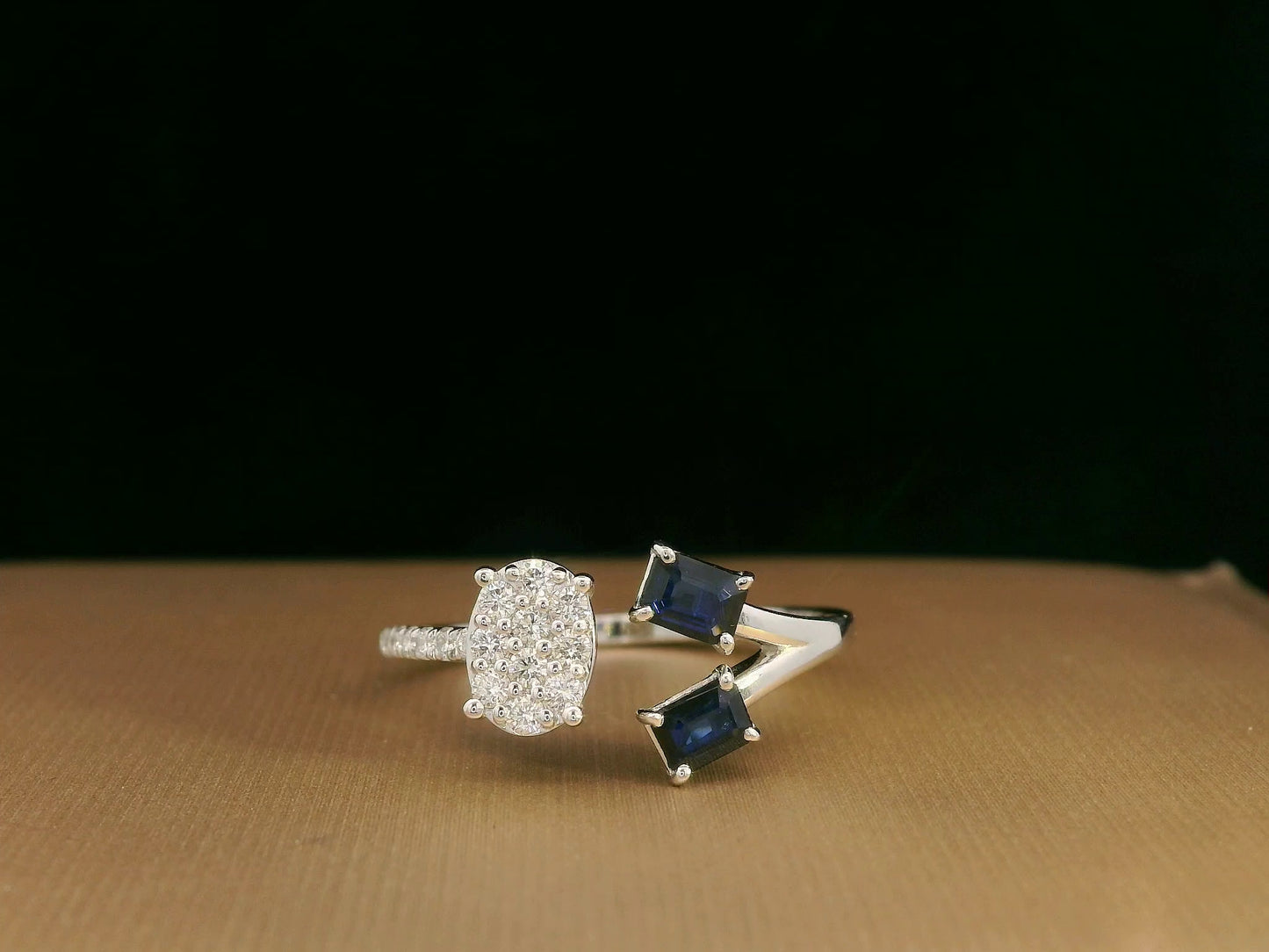 18K white gold open-shank ring featuring an oval diamond cluster on one side and two emerald-cut blue sapphires on the other, accented with pavé diamonds along the band.