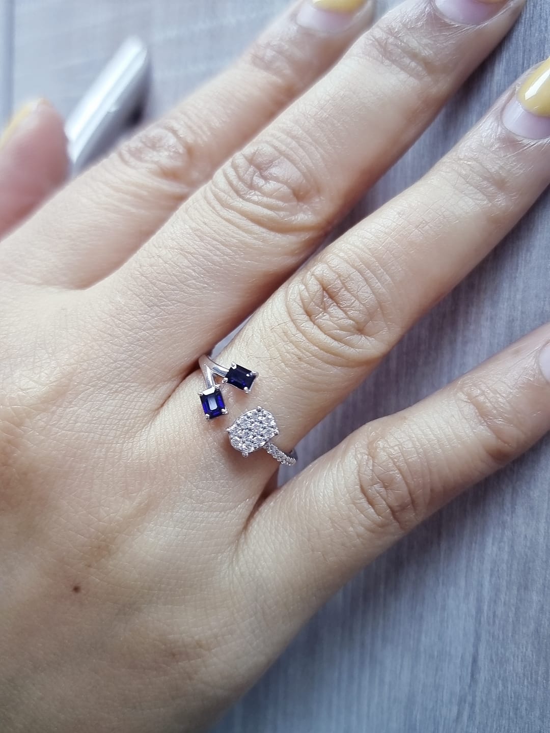 18K white gold open-shank ring featuring an oval diamond cluster on one side and two emerald-cut blue sapphires on the other, accented with pavé diamonds along the band.