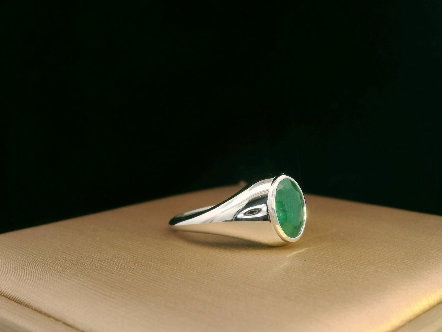 18K white gold men’s signet ring featuring a 1.80ct oval-cut emerald in a sleek bezel setting with a solid tapered band.