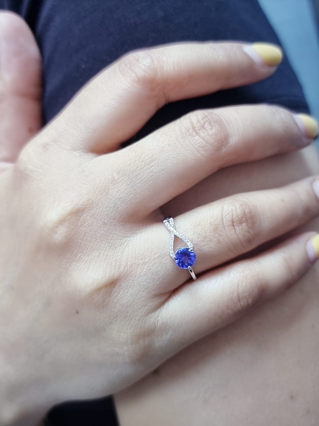 18K white gold ring featuring a 0.72ct round-cut tanzanite with 0.10ct criss-cross diamond accent band on one side and a smooth polished band on the other.