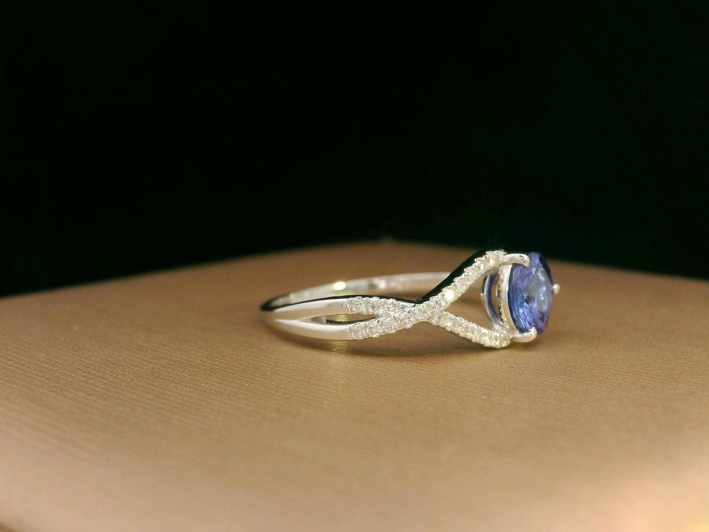 18K white gold ring featuring a 0.72ct round-cut tanzanite with 0.10ct criss-cross diamond accent band on one side and a smooth polished band on the other.