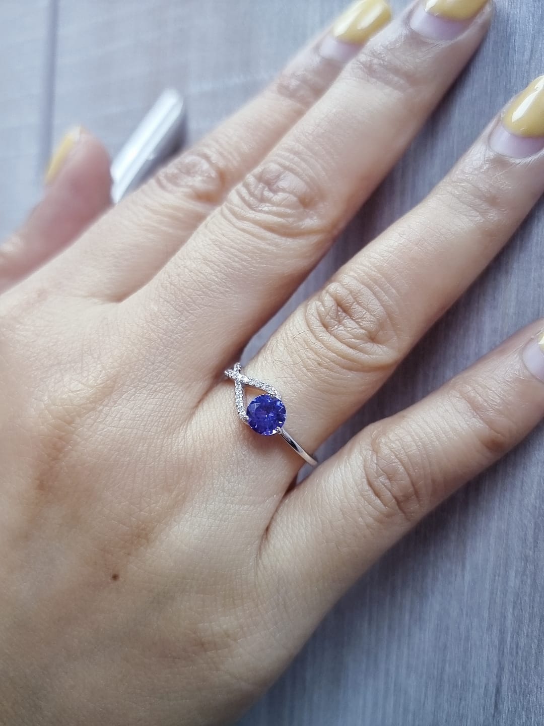 18K white gold ring featuring a 0.72ct round-cut tanzanite with 0.10ct criss-cross diamond accent band on one side and a smooth polished band on the other.