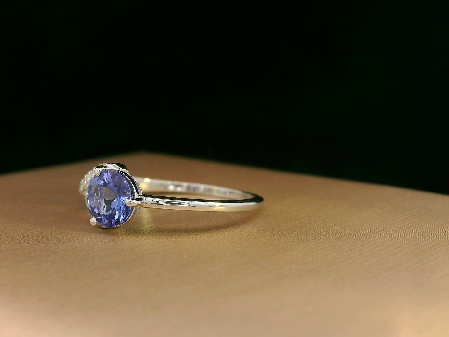 18K white gold ring featuring a 0.72ct round-cut tanzanite with 0.10ct criss-cross diamond accent band on one side and a smooth polished band on the other.