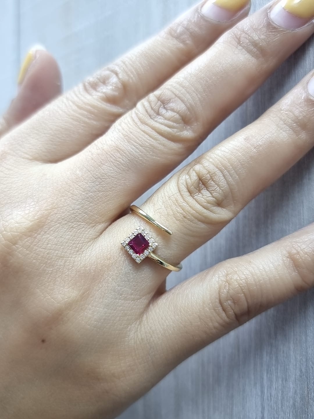 18K yellow gold ring featuring a 0.36ct square-cut ruby with 0.08ct diamonds in a halo setting on a contemporary open-bypass band.