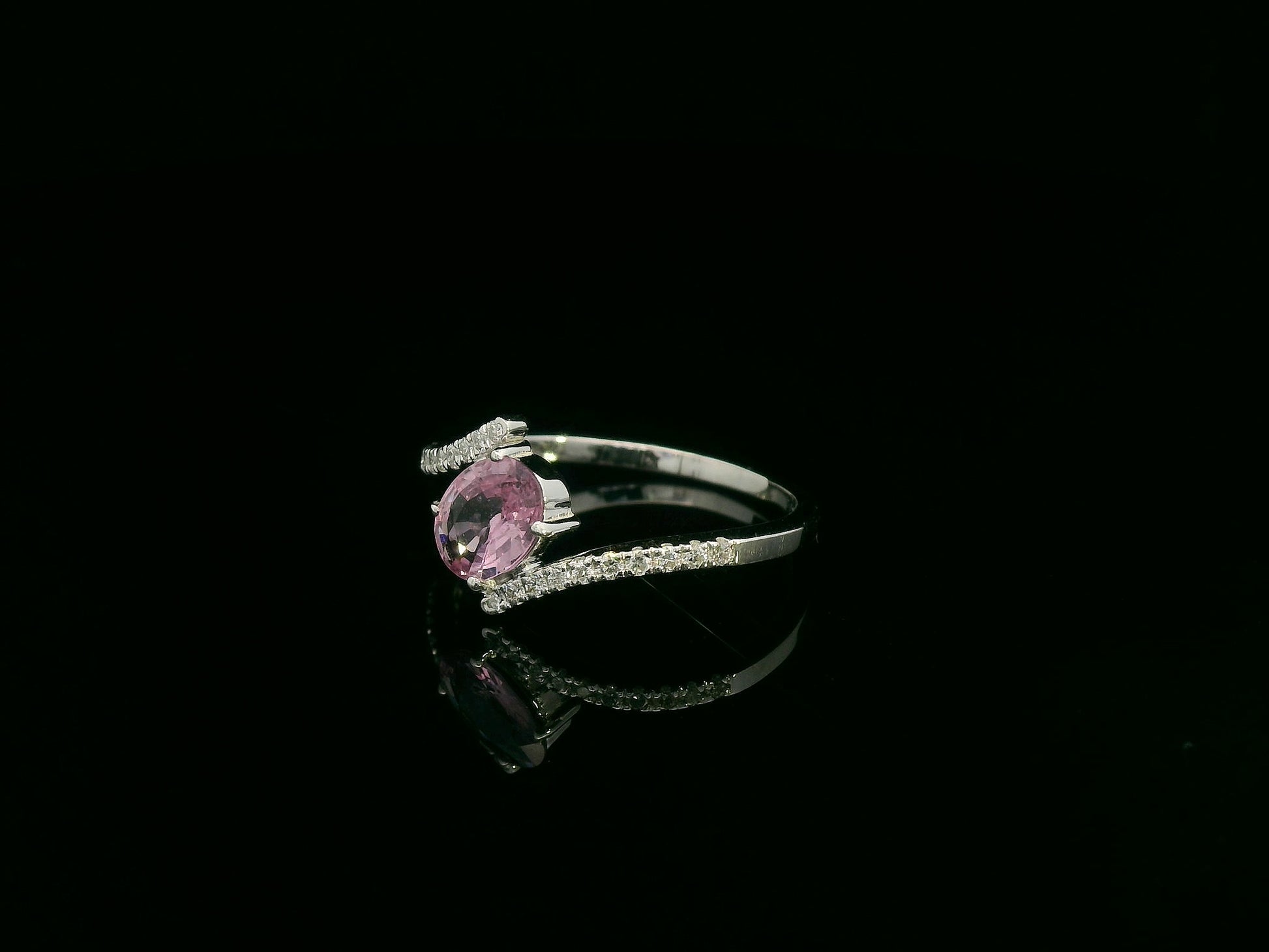 18K white gold bypass ring featuring an oval pink sapphire and pavé-set diamonds in a contemporary open design.