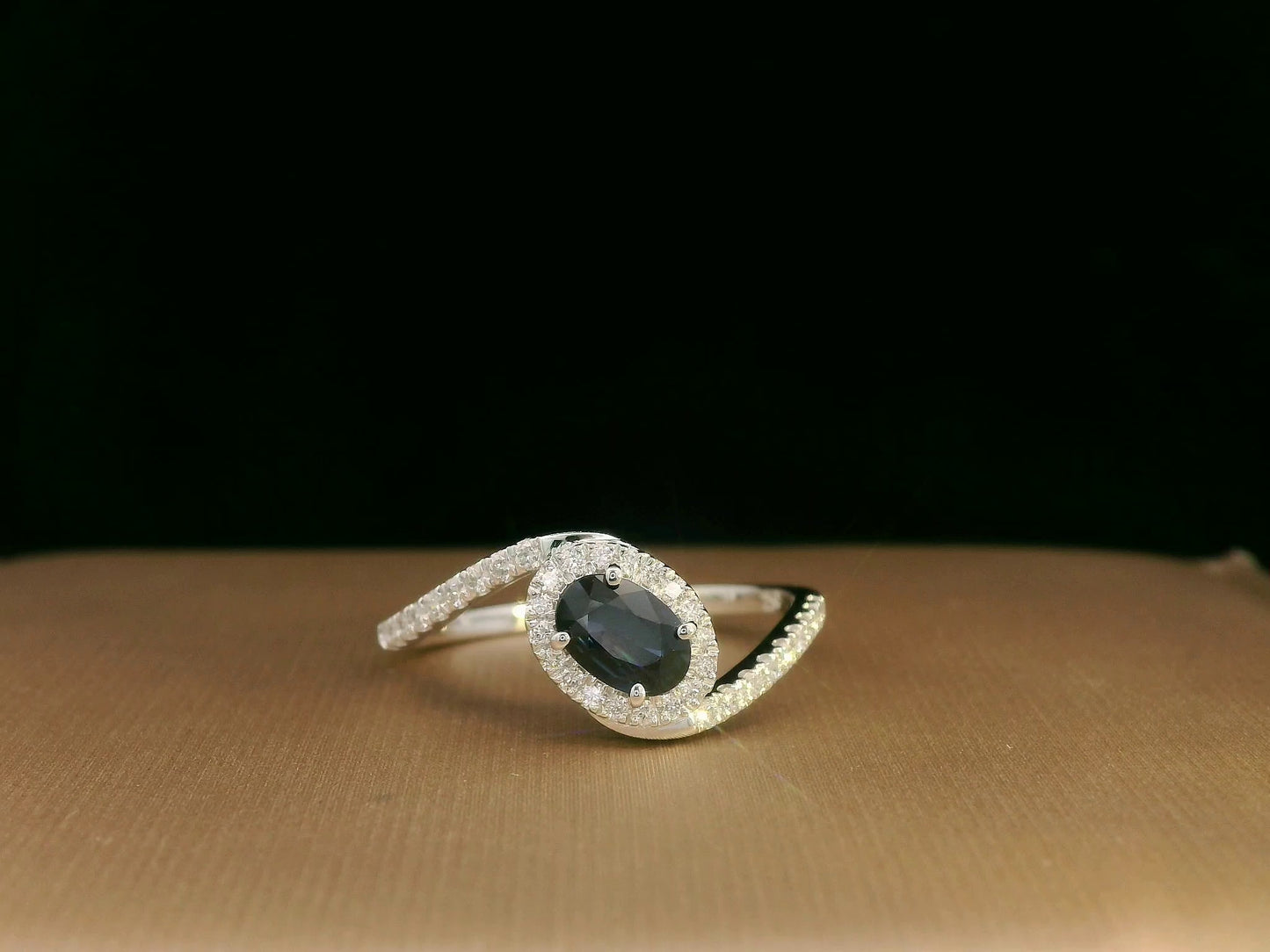 Oval blue sapphire halo ring with pavé diamonds in 18K white gold, bypass design