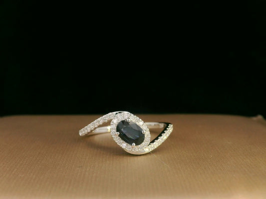 Oval blue sapphire halo ring with pavé diamonds in 18K white gold, bypass design