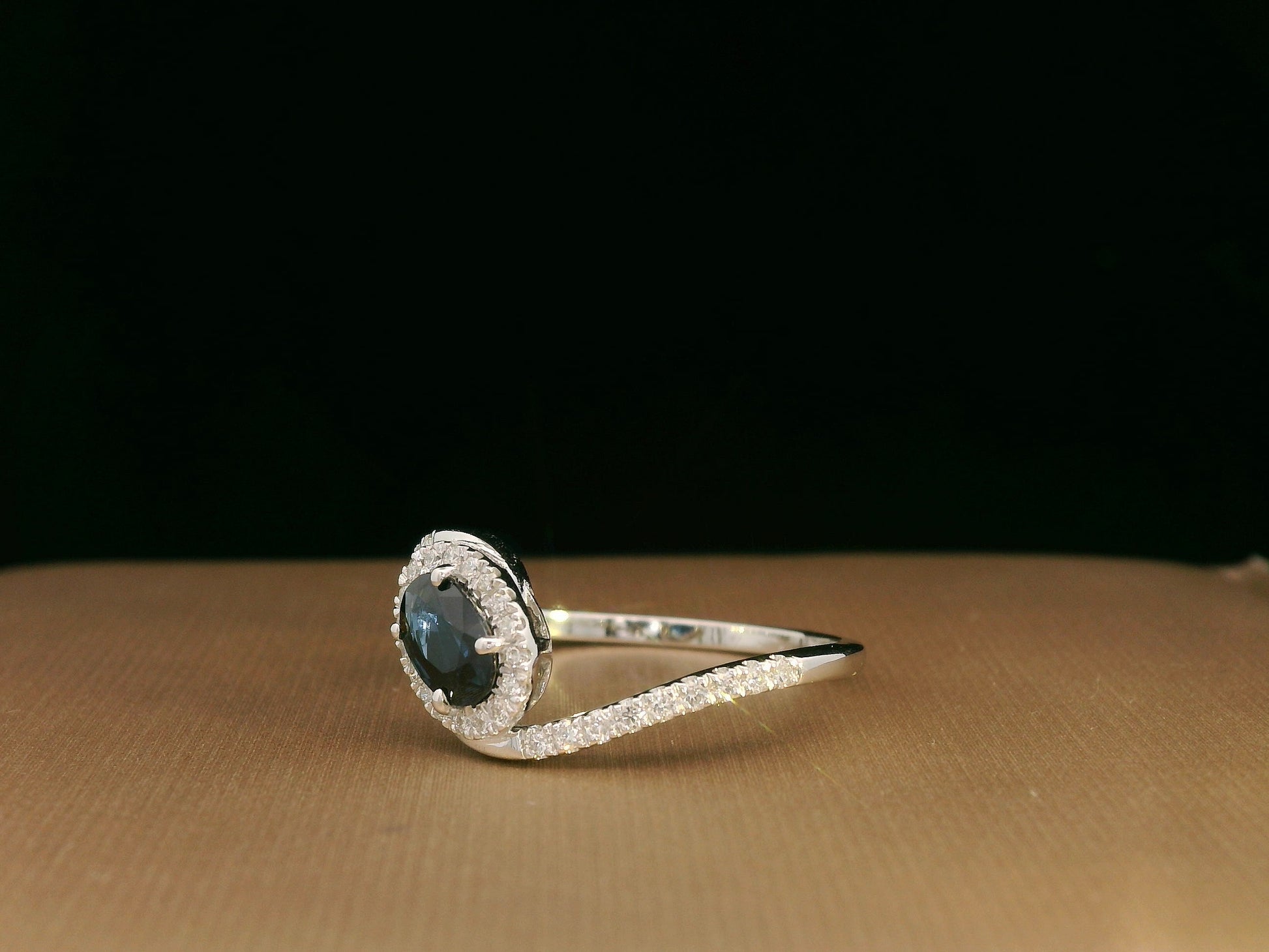Oval blue sapphire halo ring with pavé diamonds in 18K white gold, bypass design