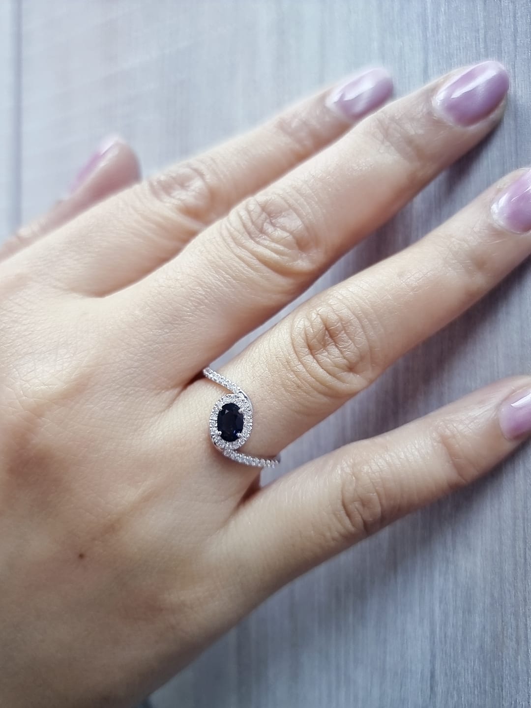 Oval blue sapphire halo ring with pavé diamonds in 18K white gold, bypass design