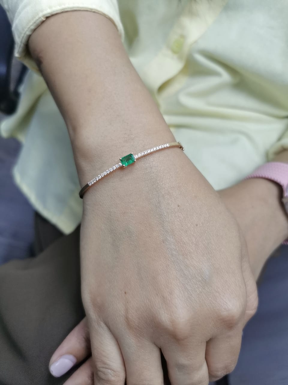 18K gold bangle with emerald-cut 0.50 carat green emerald and 0.34 carat round diamonds in a hinged bracelet design.