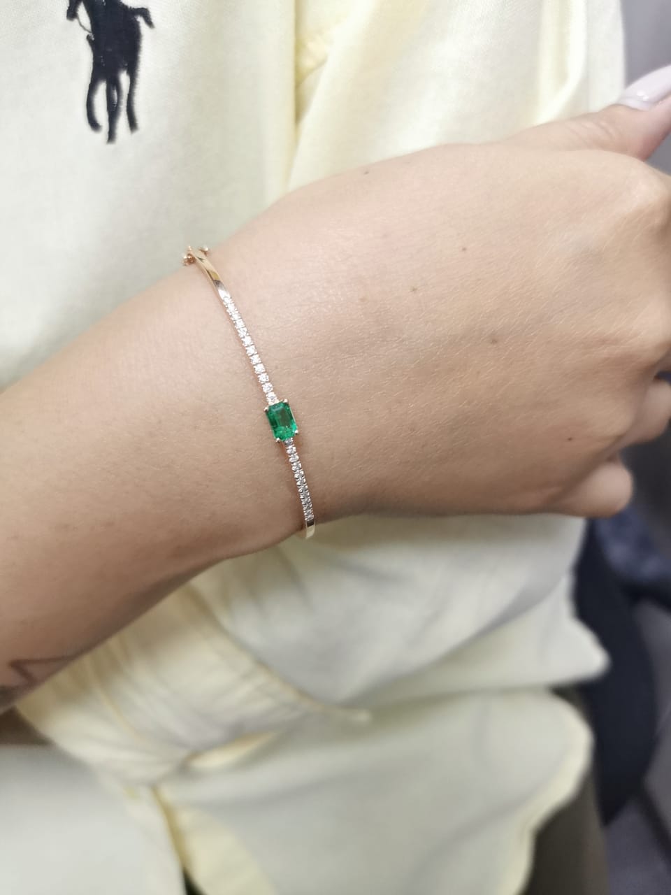 18K gold bangle with emerald-cut 0.50 carat green emerald and 0.34 carat round diamonds in a hinged bracelet design.