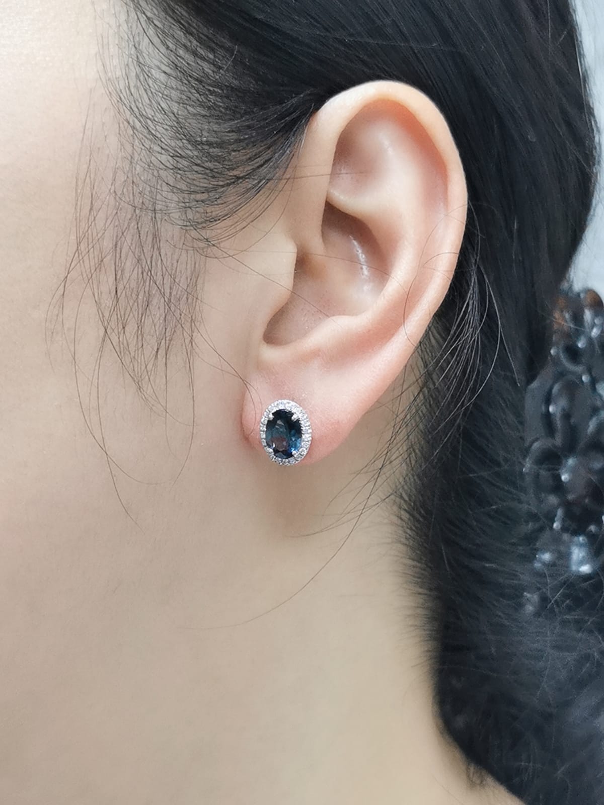 18K gold stud earrings featuring 2.90 carats of oval London Blue Topaz, encircled by a 0.25-carat diamond halo. Classic elegance with secure push-back closure.