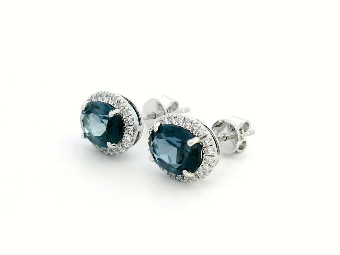 18K gold stud earrings featuring 2.90 carats of oval London Blue Topaz, encircled by a 0.25-carat diamond halo. Classic elegance with secure push-back closure.