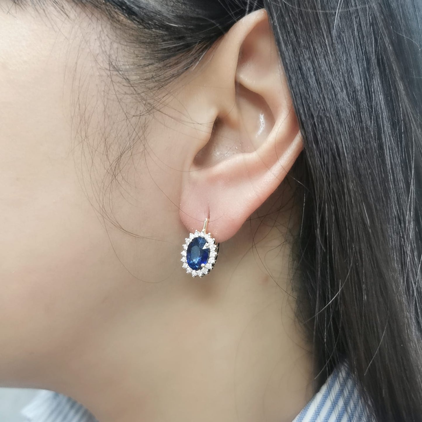 18K gold earrings featuring oval-cut Blue Sapphires (4.36ct) surrounded by a 0.56ct diamond halo, secured with hinged lever-back closures for a comfortable and elegant fit.