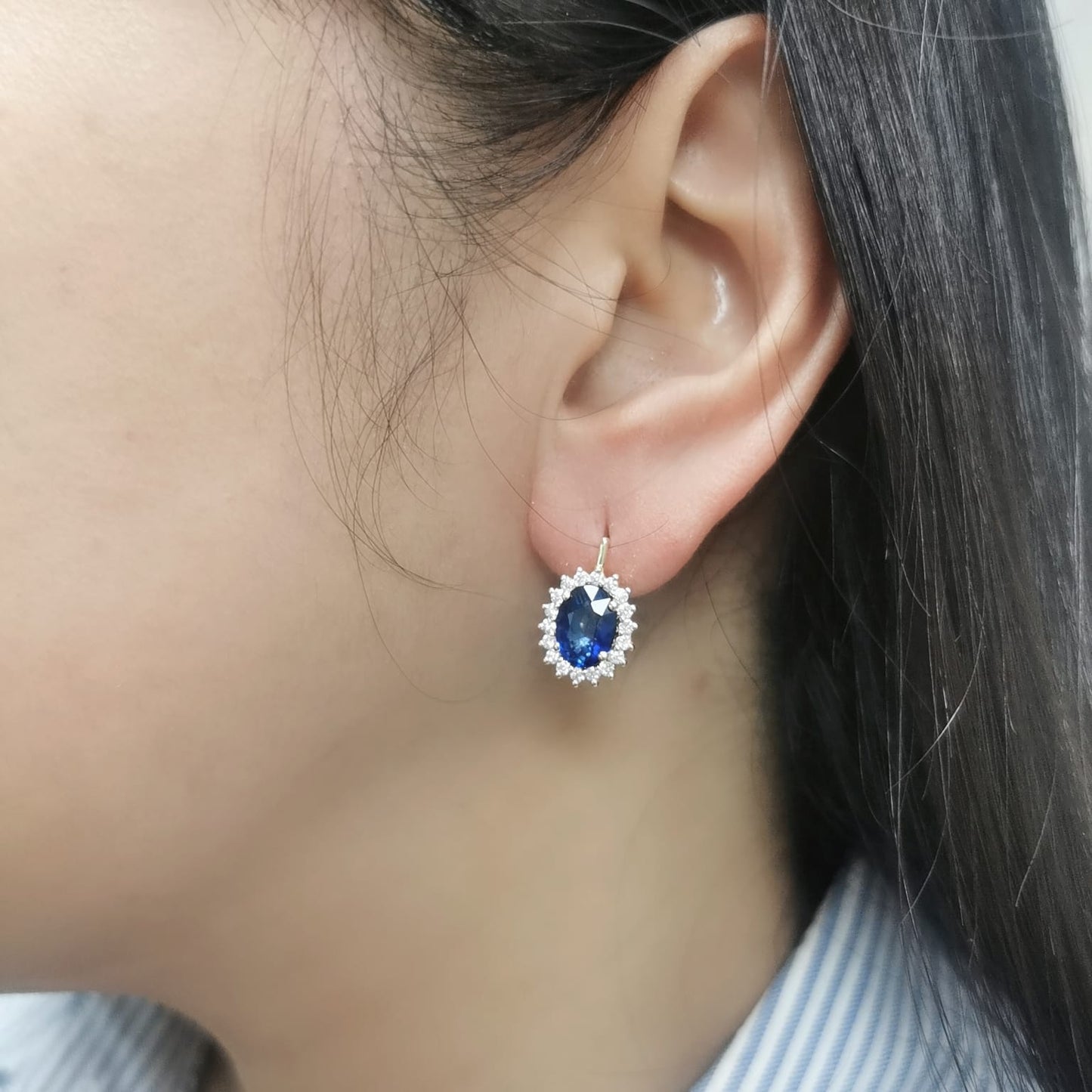 18K gold earrings featuring oval-cut Blue Sapphires (4.36ct) surrounded by a 0.56ct diamond halo, secured with hinged lever-back closures for a comfortable and elegant fit.