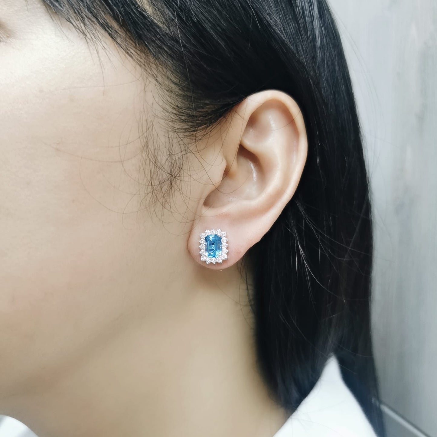 Emerald-cut blue topaz stud earrings framed by a scalloped diamond halo in 18K gold