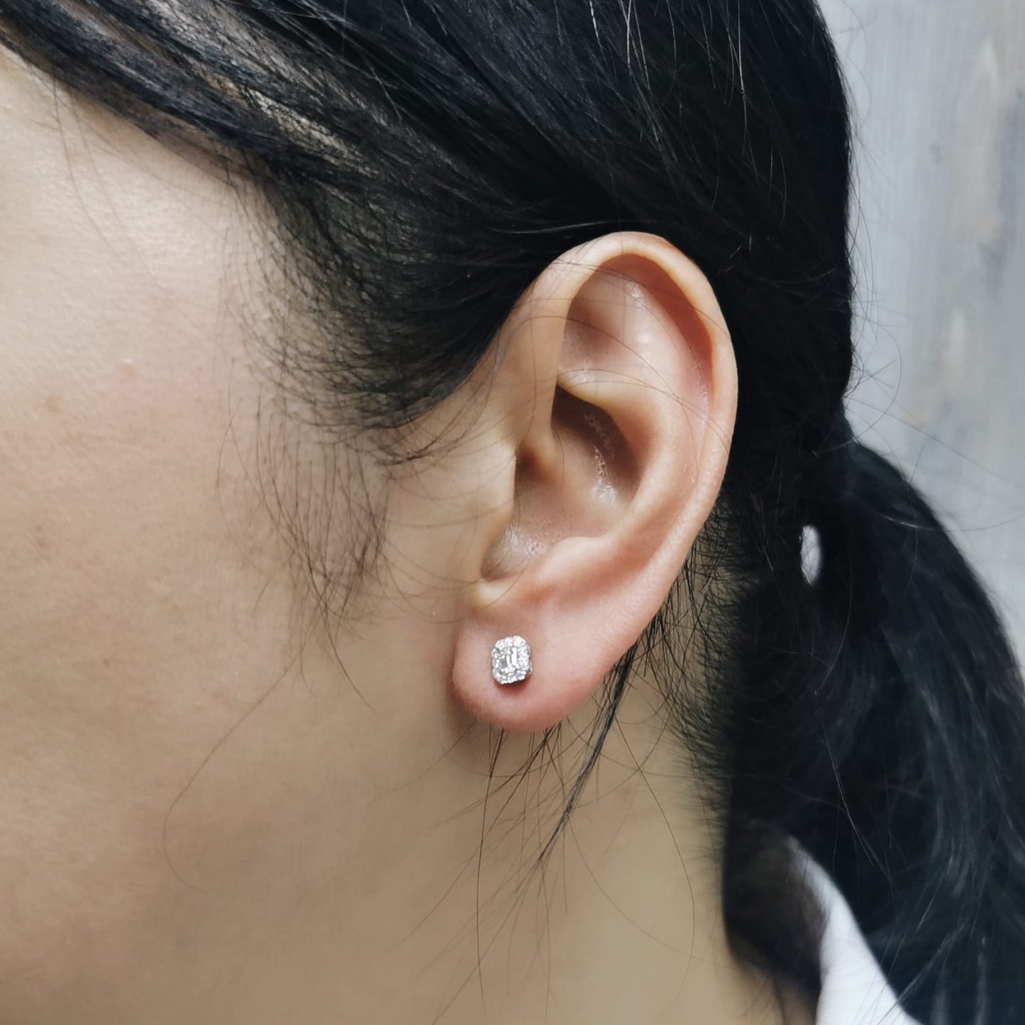 18K gold emerald-cut diamond halo stud earrings with round diamond accents, screw-back style on black background.